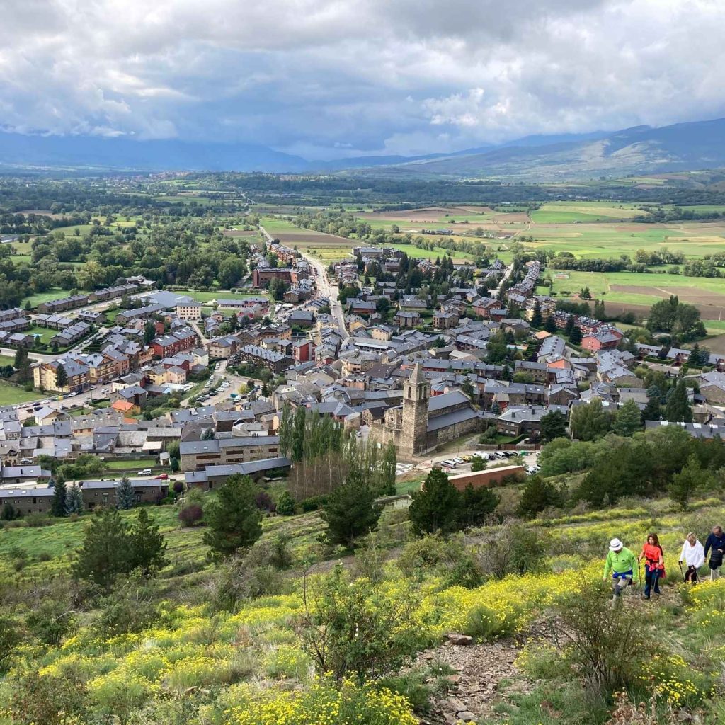 Vista aèria de Llívia i la plana de la Cerdanya des d'un sender de muntanya amb excursionistes