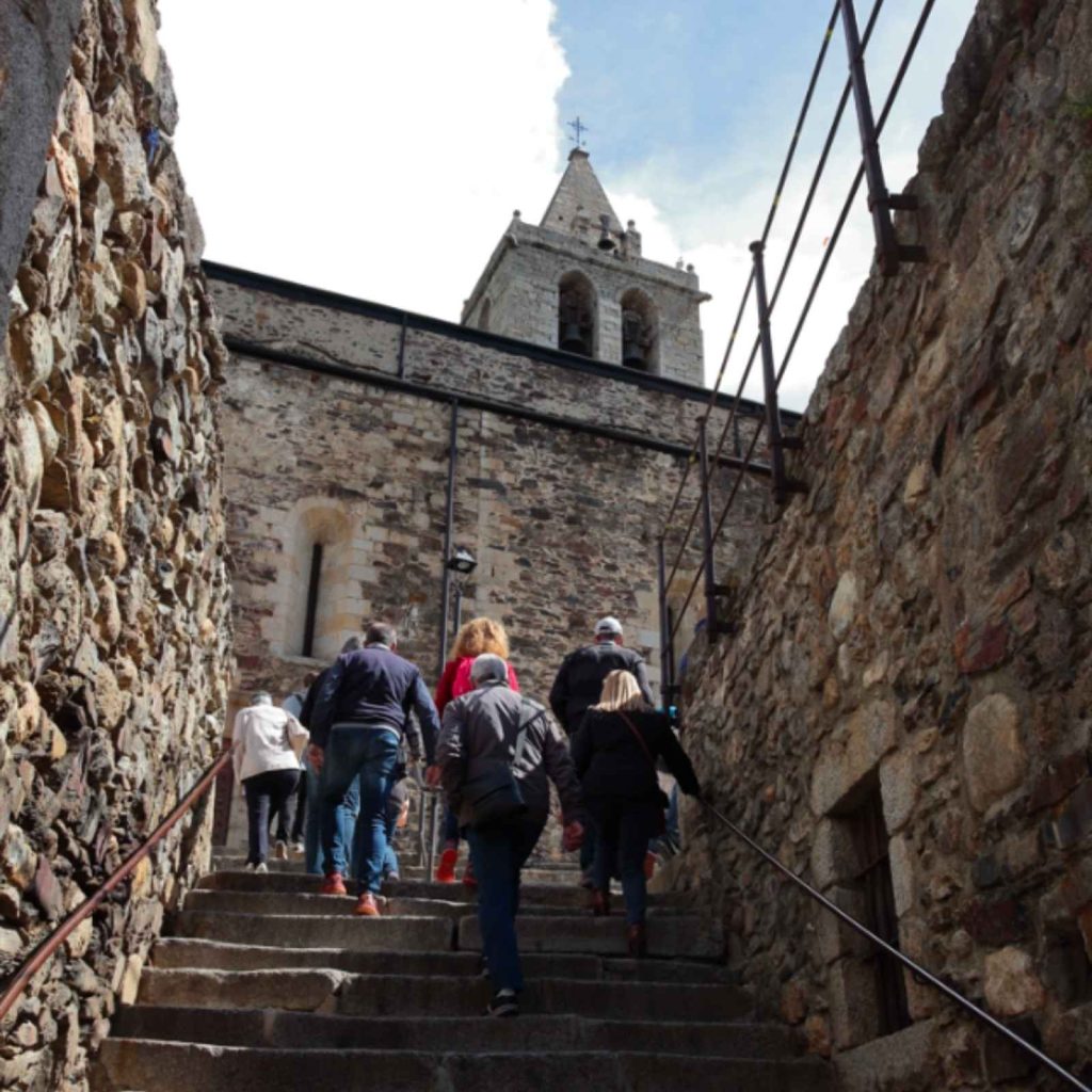 Visitants pujant les escales de pedra cap a l'església de Llívia amb el campanar al fons