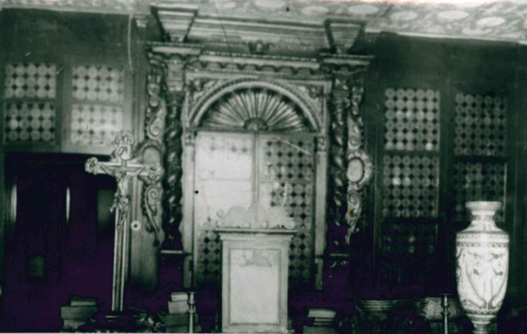 Fotografia històrica en blanc i negre de l'interior original de la Farmàcia Esteva, amb crucifix i taulell d'època